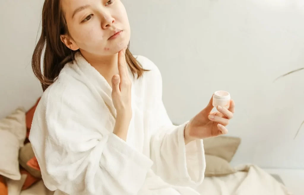 A woman wearing a robe applying facial cream - Best Skincare Products For Acne-Prone Skin