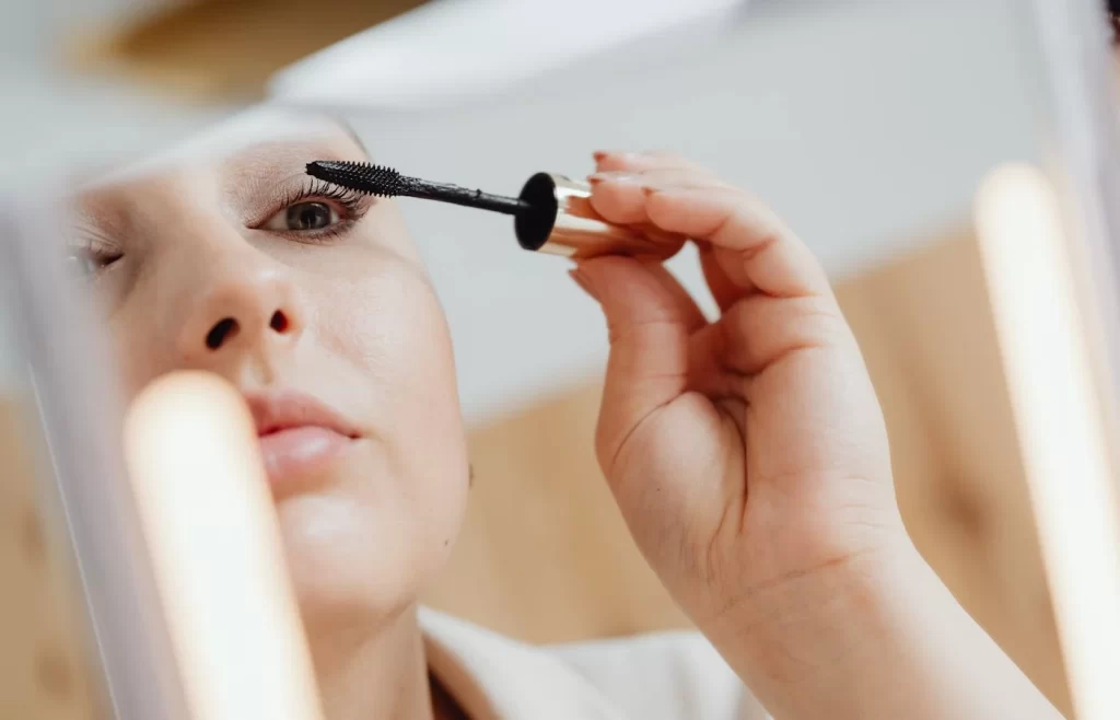 A woman mirror reflection while applying mascara - Best Makeup Products For Beginners