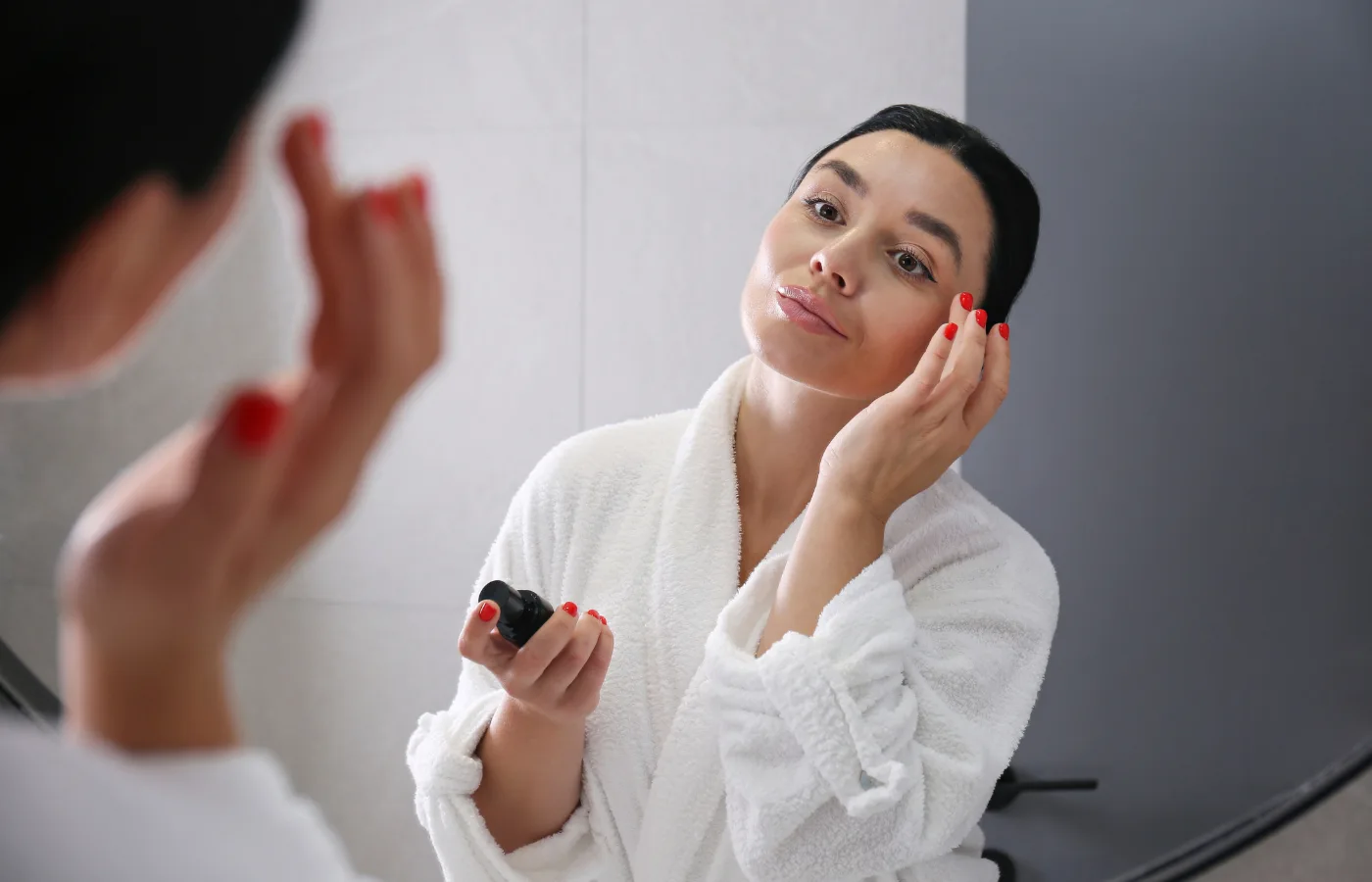 Woman putting on skincare against mirror. - Best Gentle Retinol For Beginners