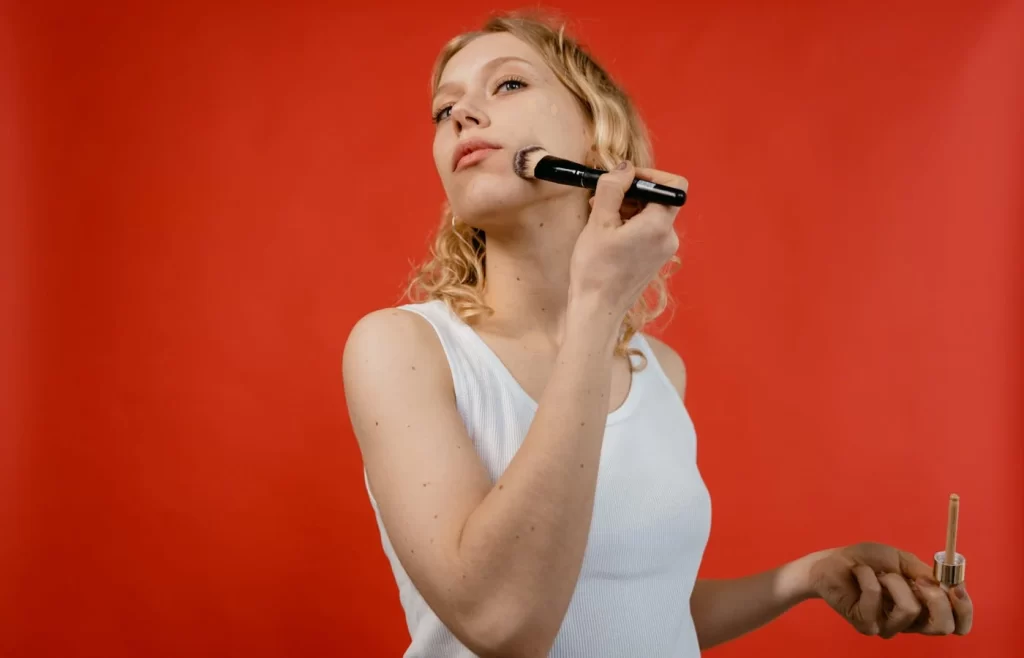 Woman in white tank top applying foundation - Foundations For Oily Skin