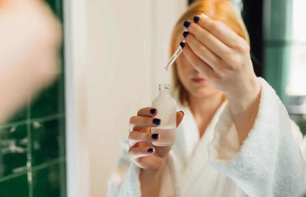 Reflection of woman holding a bottle of serum - Top 10 Skin Care Tips For Summer