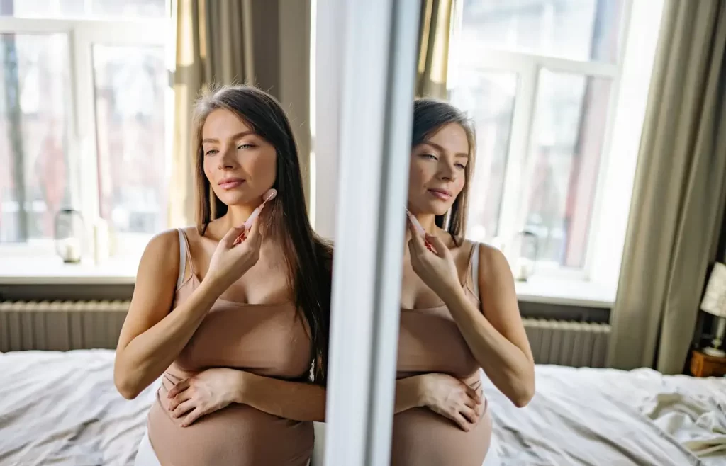 A pregnant woman using a face roller - Pregnancy Skincare Routine