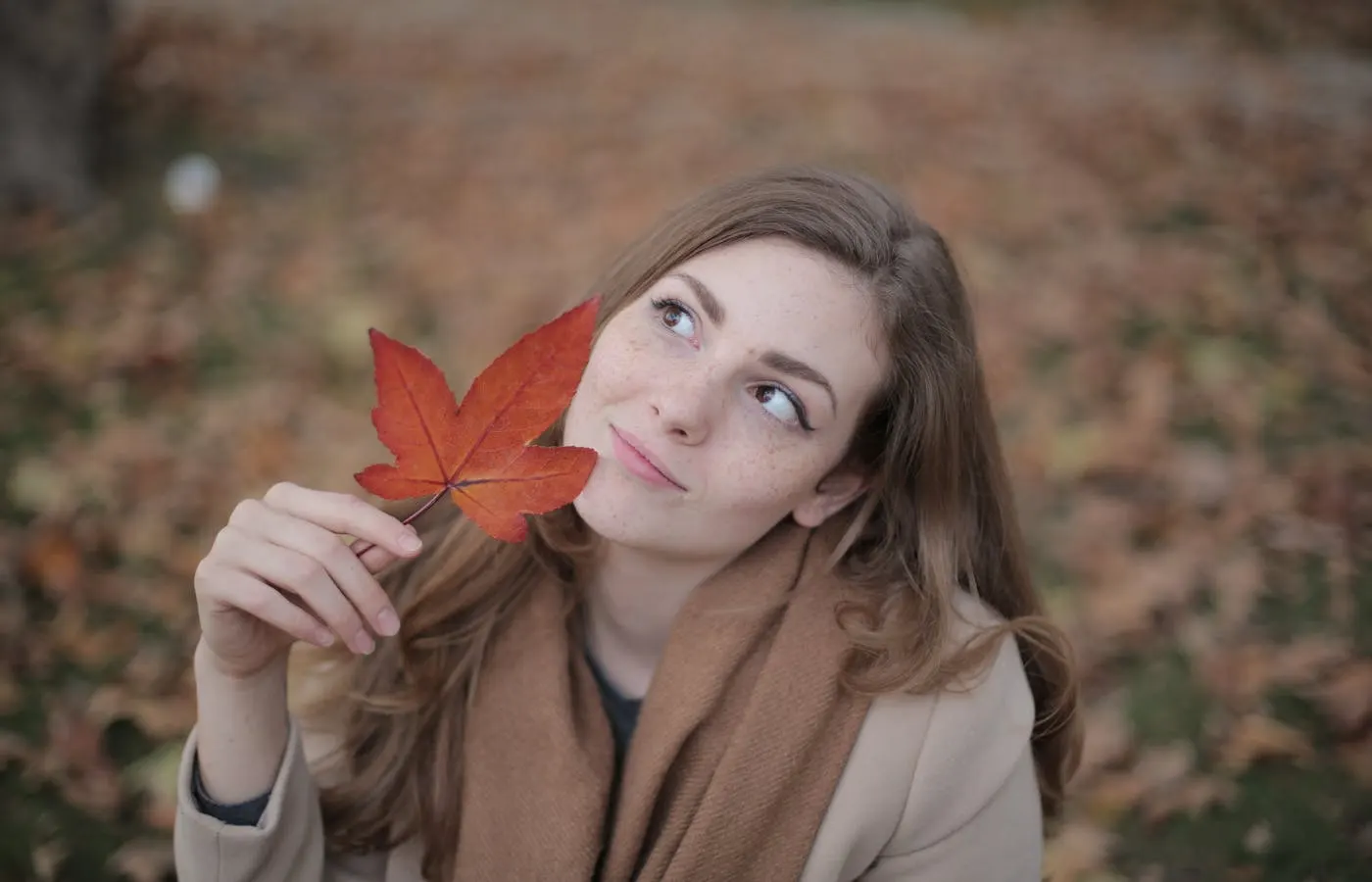 Woman in Brown Coat Holding Red Maple Leaf - Fall Skin Care Tips