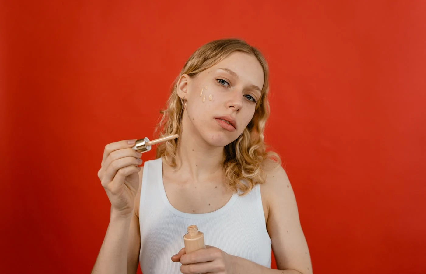 Woman in a white tank top applying foundation on face - How To Apply Makeup On Dry Skin