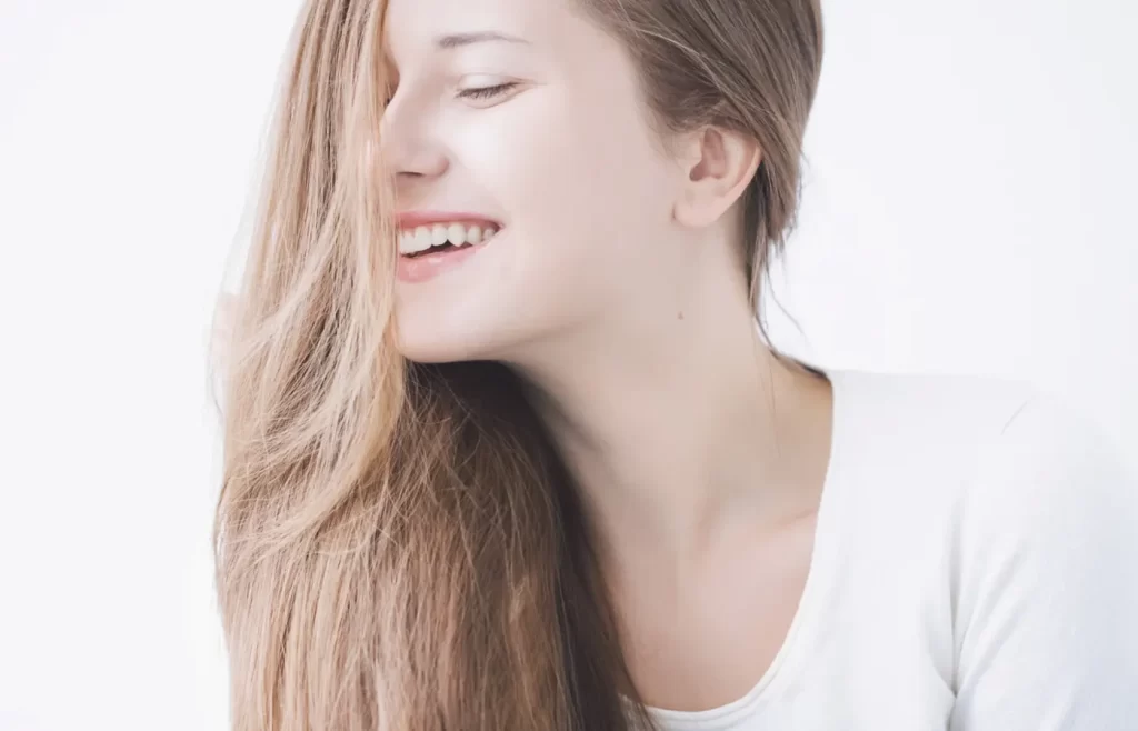 Close up of a blond woman in a white top smiling -hair care routine for low porosity hair